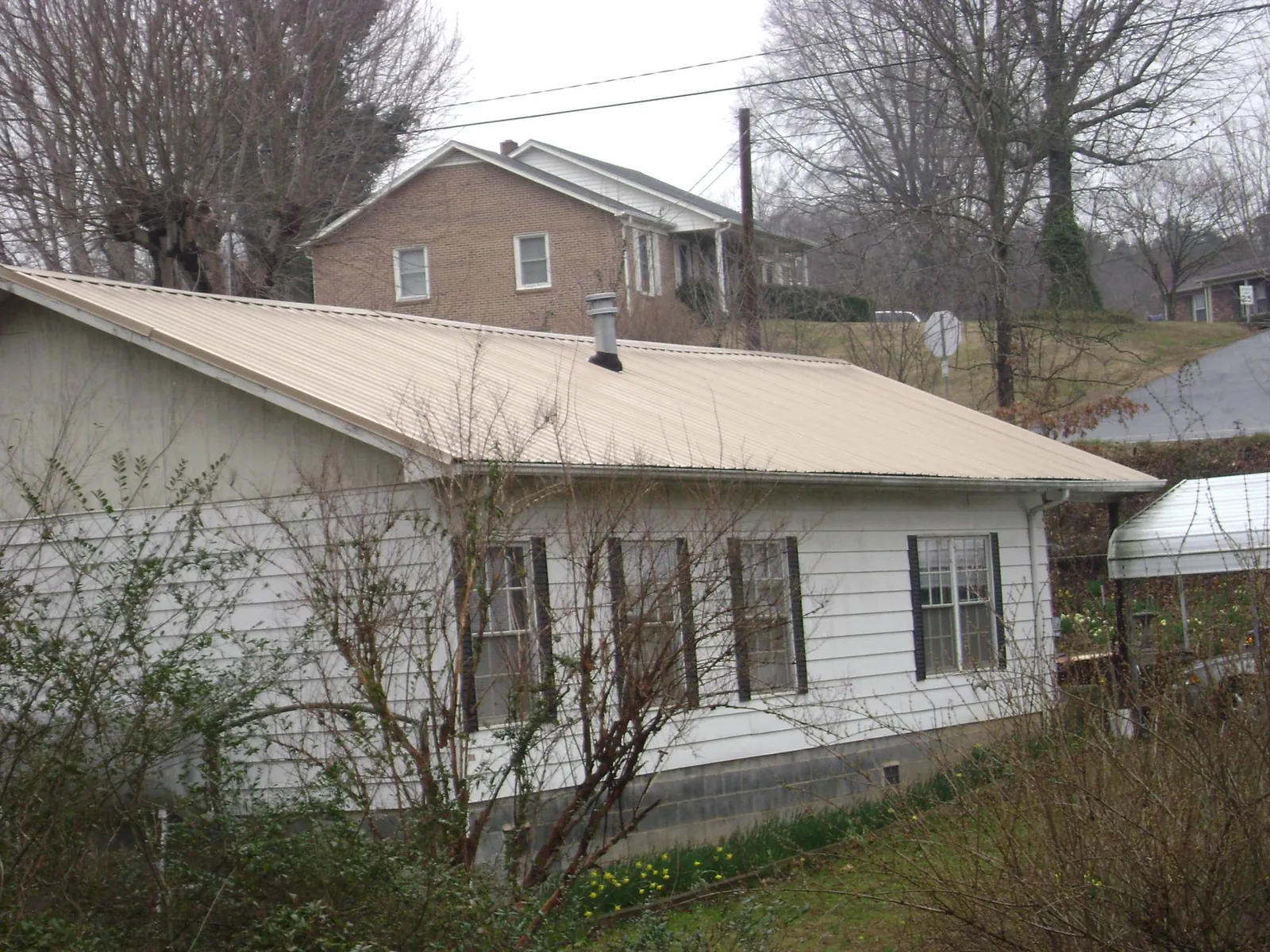 Tan metal roof on a white sided house set into a hillside — Commercial Roofing by Roofing Brothers in Ocean Grove